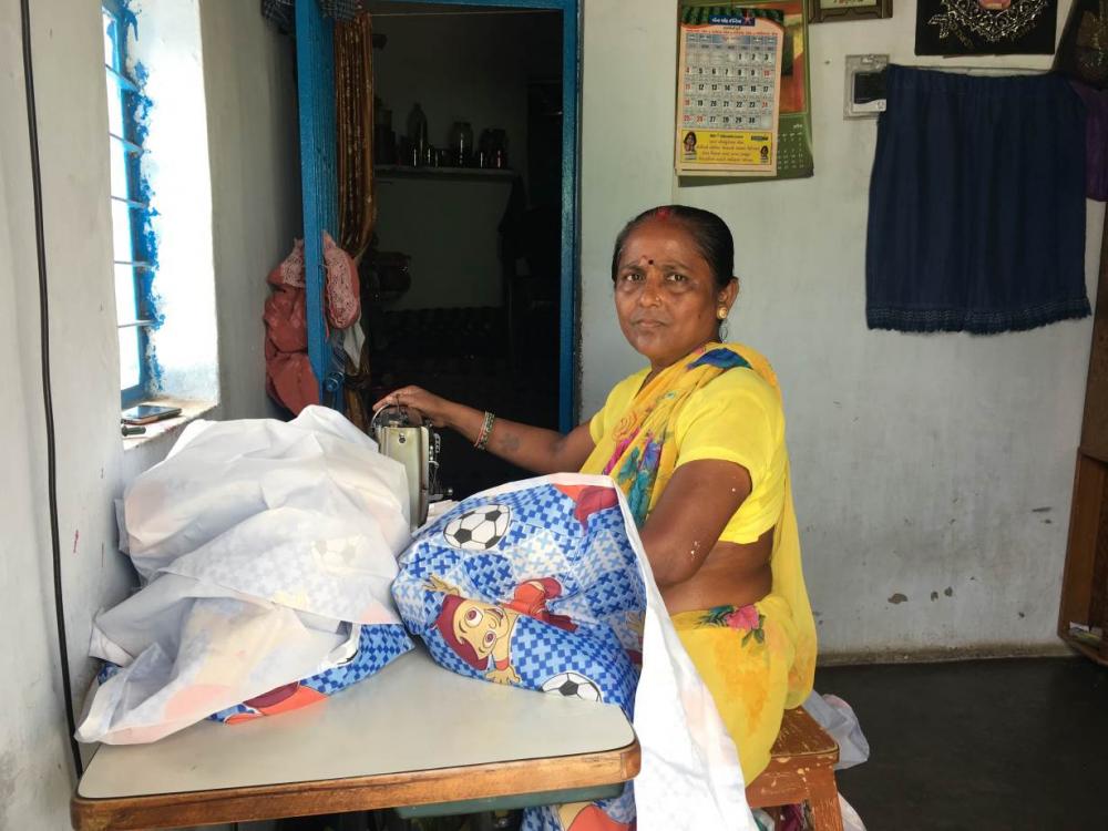Meenaben sews in her home, whose roof has been painted with reflective paint to reduce summer temperatures as slum communities build resilience against climate change in Ahmedabad, India. (Photo source: Thomson Reuters Foundation/Rina Chandran)